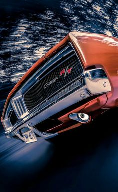 the front end of a red sports car driving on a road with water in the background