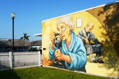 a mural on the side of a building depicting an elderly woman holding a camera and looking through it