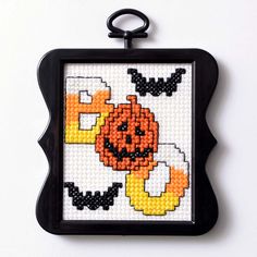 a cross stitch pattern with a black frame holding a pumpkin on it's face