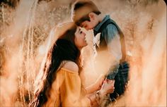 a man and woman standing in tall grass with their heads touching each other's foreheads