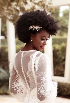 a woman with an afro wearing a white dress and flowers in her hair is standing outside