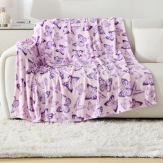 a white couch with a purple blanket on it in front of a white rug and wall