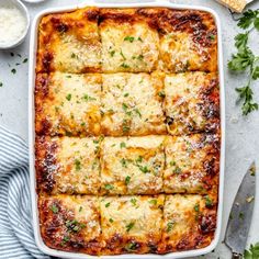 a casserole dish with cheese and parmesan on top, surrounded by utensils