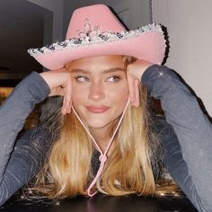 a woman wearing a pink cowboy hat sitting at a table with her hands on her head