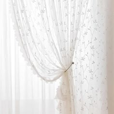 a white curtain with flowers on it in front of a window