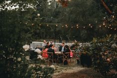 a group of people sitting around a wooden table in the middle of a forest at night