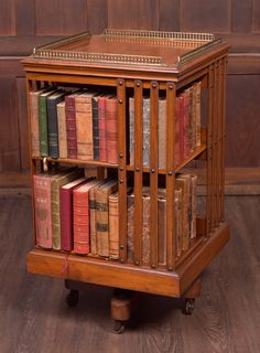 an old wooden book shelf with many books on it's sides and wheels, in front of a wood paneled wall