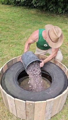 a man in a hat is pouring water into an old barrel with grass and bushes behind him