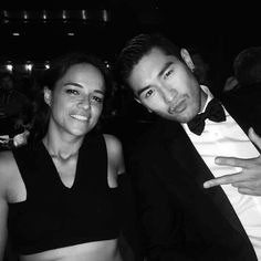 a man and woman posing for a photo in formal wear at a party with one pointing to the camera