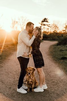 a man and woman standing next to a brown dog on a dirt road with the sun behind them