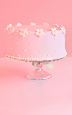 a pink cake with white flowers on top sitting on a glass stand in front of a pink background