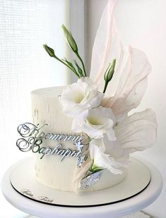 there is a white cake with flowers on the top and silver lettering on the bottom