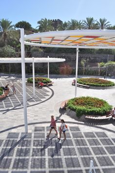 two people walking in the middle of a circular courtyard with plants and umbrellas over it