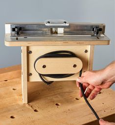 a person holding a black cord in front of a wooden table with a machine attached to it