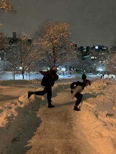 two people running in the snow at night with buildings in the backgrouds