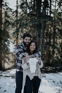 a man and woman are standing in the snow holding a sign that says love is all around them