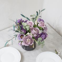 a vase filled with purple flowers sitting on top of a table next to two white plates