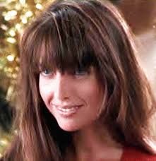 a woman with long brown hair and bangs smiling at the camera while standing in front of a christmas tree