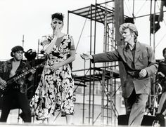 a man and woman standing on stage with their hands in the air as they sing