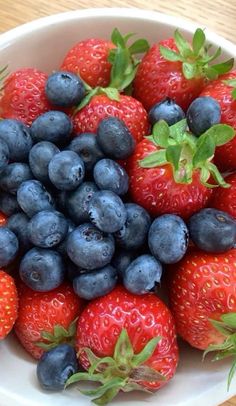 a bowl filled with blueberries and strawberries on top of a wooden table,