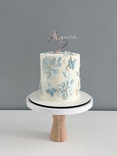 a white cake with blue flowers and the number two on top is sitting on a wooden stand