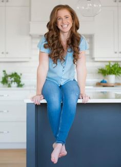 a woman sitting on top of a kitchen counter next to a blue cabinet and white cabinets