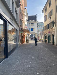 a person is walking down the street in front of some buildings and shops on a sunny day