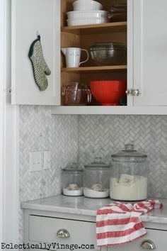 a kitchen with white cupboards and dishes on the counter top, next to a red and white dish towel