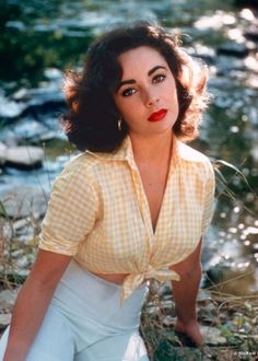 a woman in yellow shirt and white pants posing for a photo by the riverbank