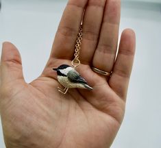 a small bird sitting on top of a person's hand wearing a gold chain