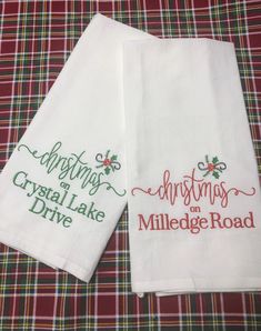 two white towels with embroidered words on them sitting on a plaid tableclothed surface