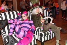 two people dressed up in costumes sitting on couches with other people standing behind them