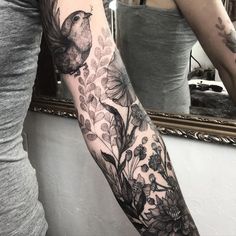 a woman's arm with a bird and flowers tattoo on her left arm, in front of a mirror