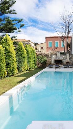 an empty swimming pool in front of a house with trees and bushes around it,