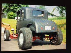 an old black truck with big tires parked in front of a house on the street