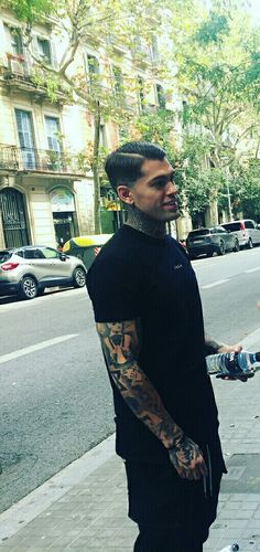 a man with tattoos on his arm standing next to a skateboard in the street