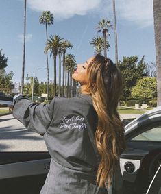 a woman standing next to a car with her hand on the door handle and palm trees in the background