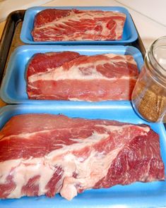 three trays filled with raw meat sitting on top of a counter next to a glass jar