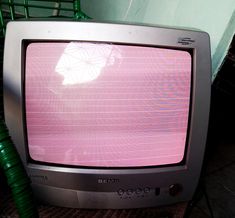 an old tv sitting on top of a wooden table next to a green wire chair