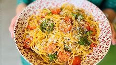 a person holding a plate of spaghetti with tomatoes and parmesan cheese