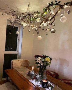 a dining room table with candles and ornaments hanging from the tree branch over it's head