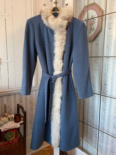 This stunning coat comes from The Sterling Stall Group in Winnipeg, Manitoba, Canada. It's made of pure virgin wool in medium blue, trimmed along the neckline and front edge with white fox fur tinged with very dark brown. The coat has the original buttons and elastic closures in the front, two front pockets and a matching tie belt, and is fully lined with thick blue satiny lining. The outside measurements, taken with the coat lying flat, are: shoulder to shoulder, 18 inches; armpit to armpit, 20 inches; sleeves, 23 inches; length, 47 inches; bottom edge, 28 inches. In very good condition. Fitted Long Wool Coat With Faux Fur Trim, Fitted Blue Fur Coat With Faux Fur Trim, Fitted Blue Winter Fur Coat, Fitted Blue Fur Coat For Winter, Blue Wool Coat, Manitoba Canada, Winnipeg Manitoba, Mink Fur Coat, Long Wool Coat