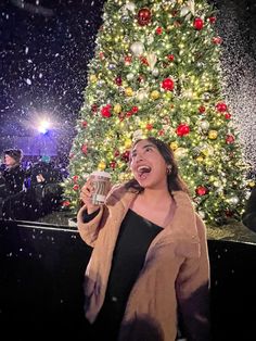 a woman standing in front of a christmas tree with her mouth open and holding a cup