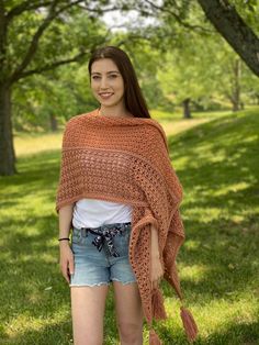 a woman standing in the grass wearing a crocheted shawl