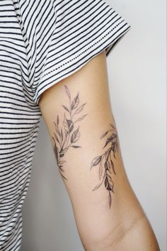 a woman with a tattoo on her arm that has leaves growing out of it and is wearing a striped shirt