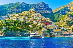 a boat is in the water near some buildings on a hill side with mountains in the background