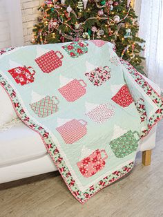 a christmas tree is next to a couch with a quilt on it and a coffee mug