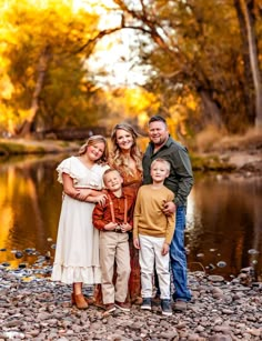 a family posing for a photo in front of a river with fall leaves on the trees