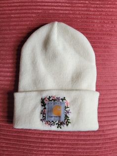 a white beanie with a flowered patch on the front and side of it