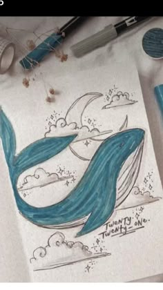 a drawing of a blue whale on paper next to markers and pencils with writing underneath it